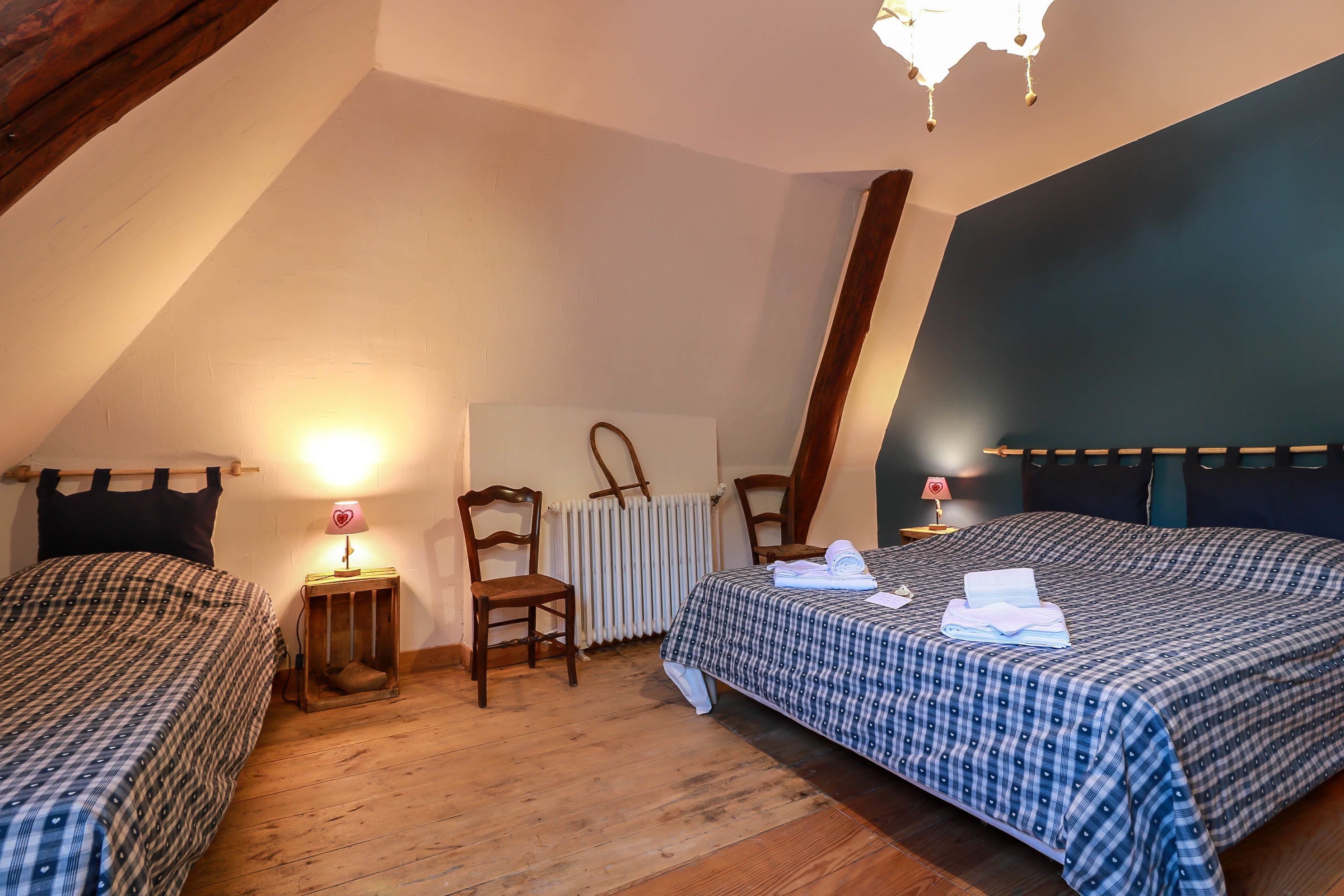 A bedroom with two beds, wooden flooring, a radiator, and a chandelier.