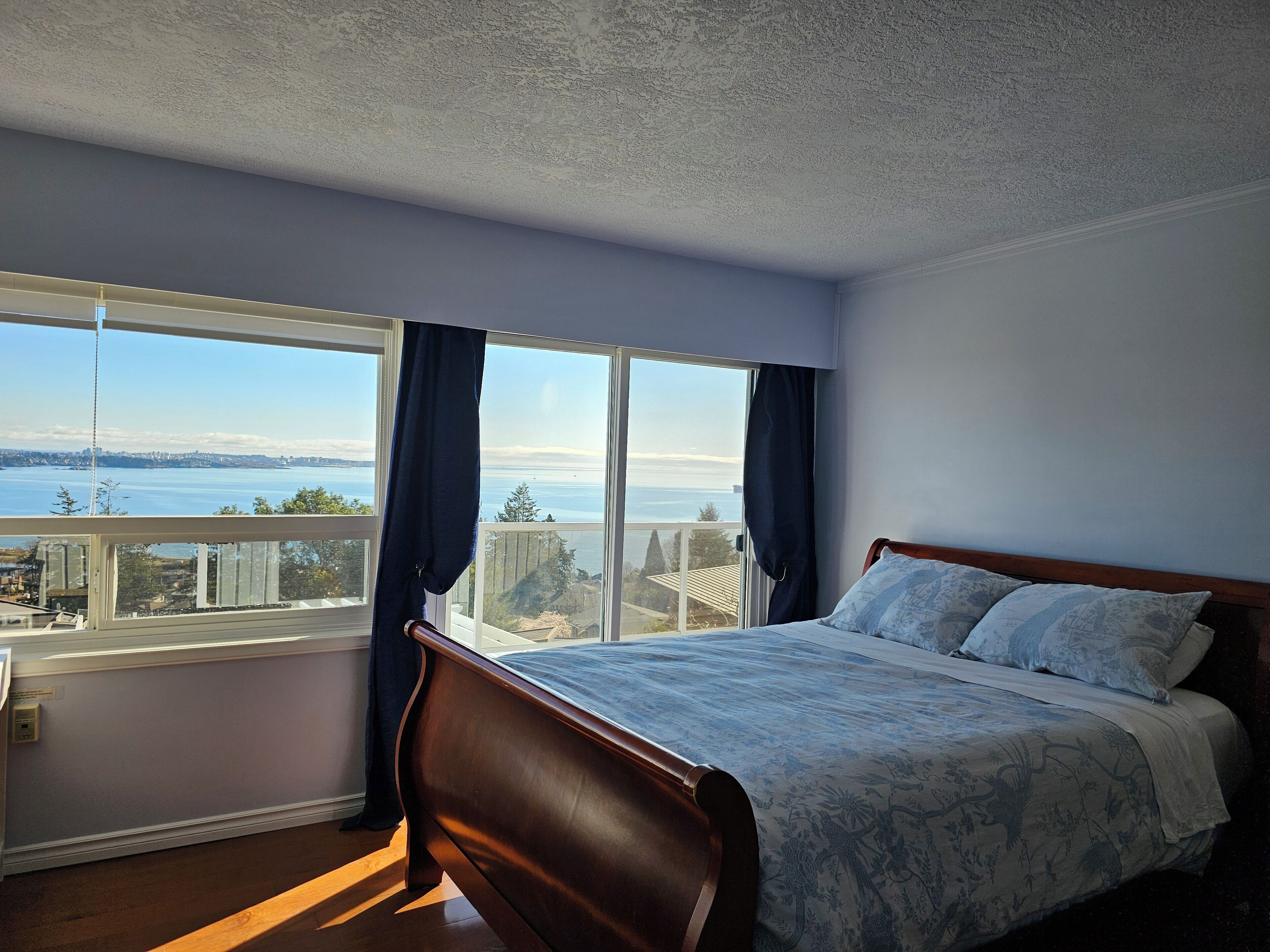 A bedroom with a large window, a wooden bed, and a view of the sea.