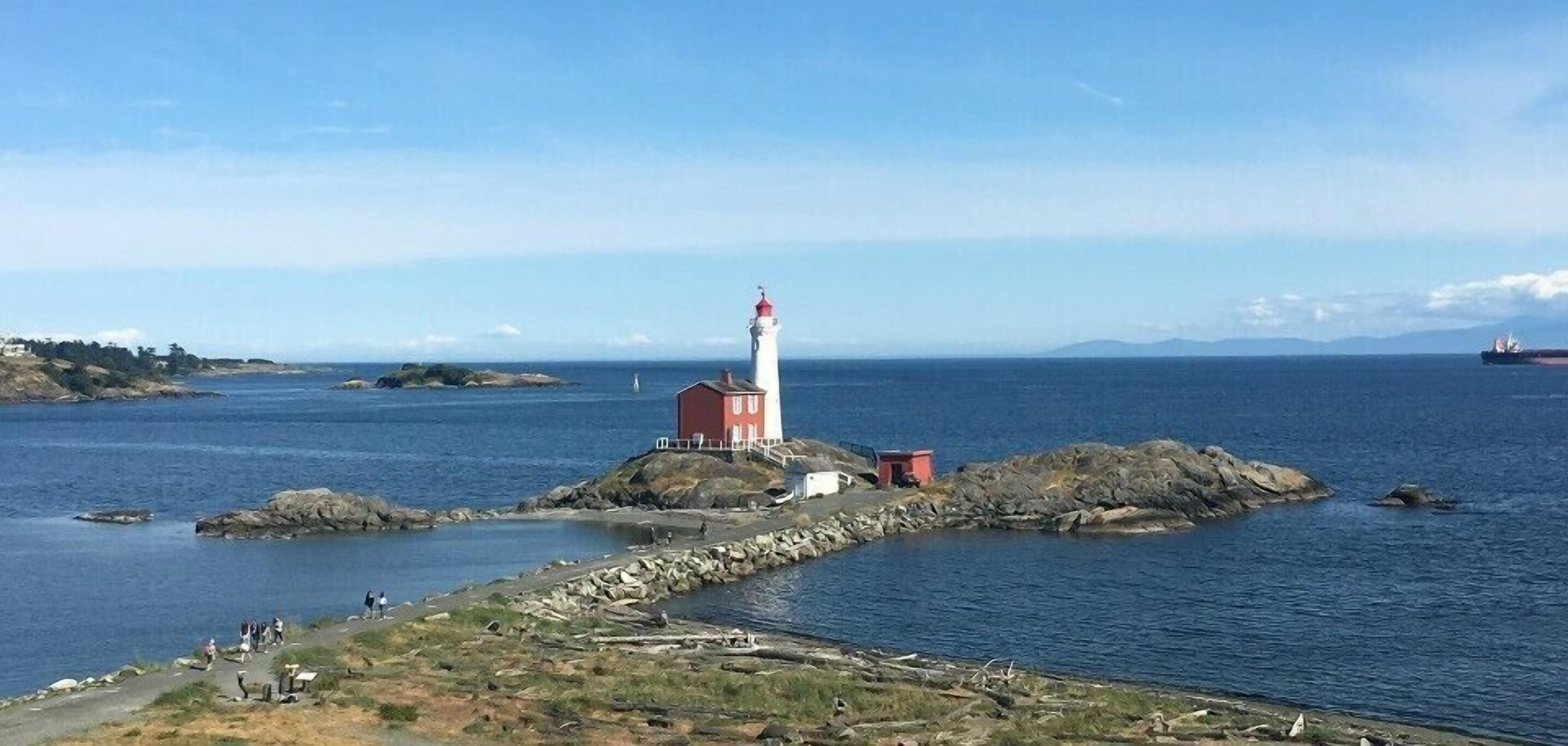 Um farol numa formação rochosa, com vista ampla para o mar e montanhas ao longe.