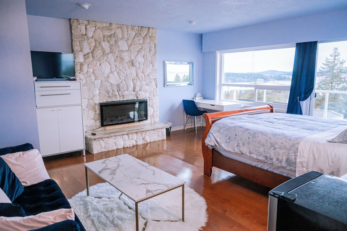 A bedroom with a stone wall, a bed, a desk, and a TV.