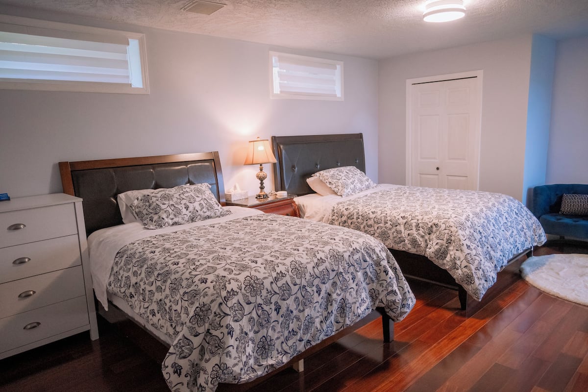 A bedroom with two beds, a nightstand with a lamp, a dresser, and a door.