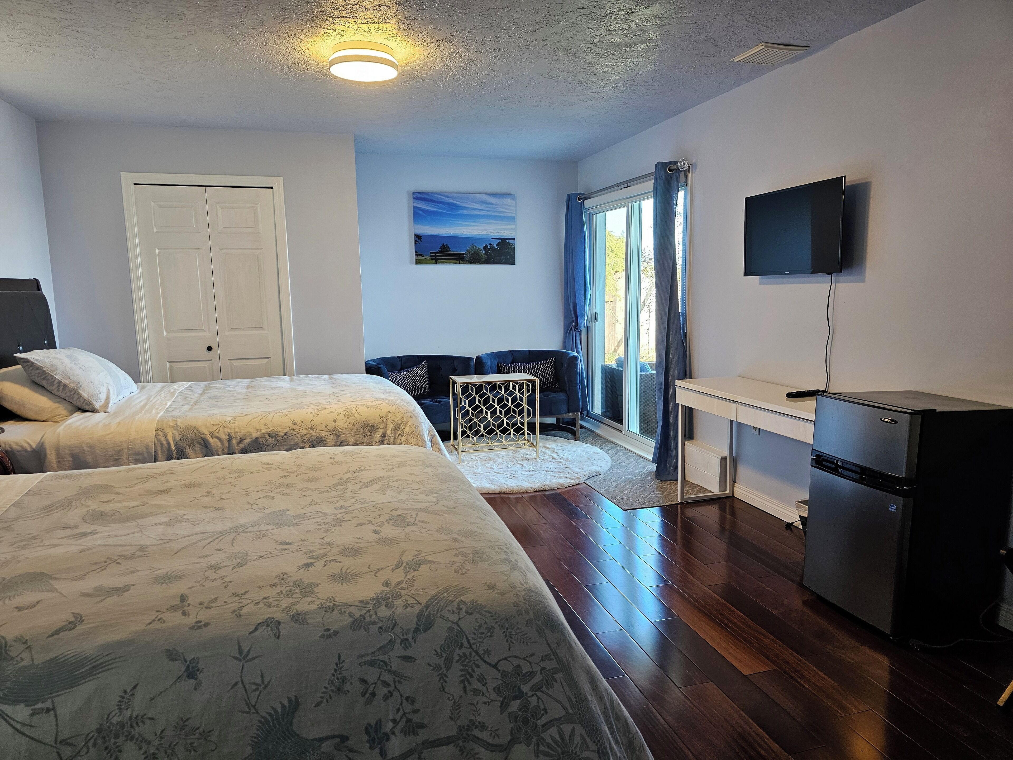 A bedroom with two beds, a desk, a refrigerator, and a TV.
