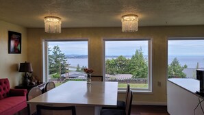 A dining area with a large table, two chandeliers, a red sofa, and a view of the sea through large windows. - HOV B&B House -Hospitality Ocean view Victoria- (Victoria)