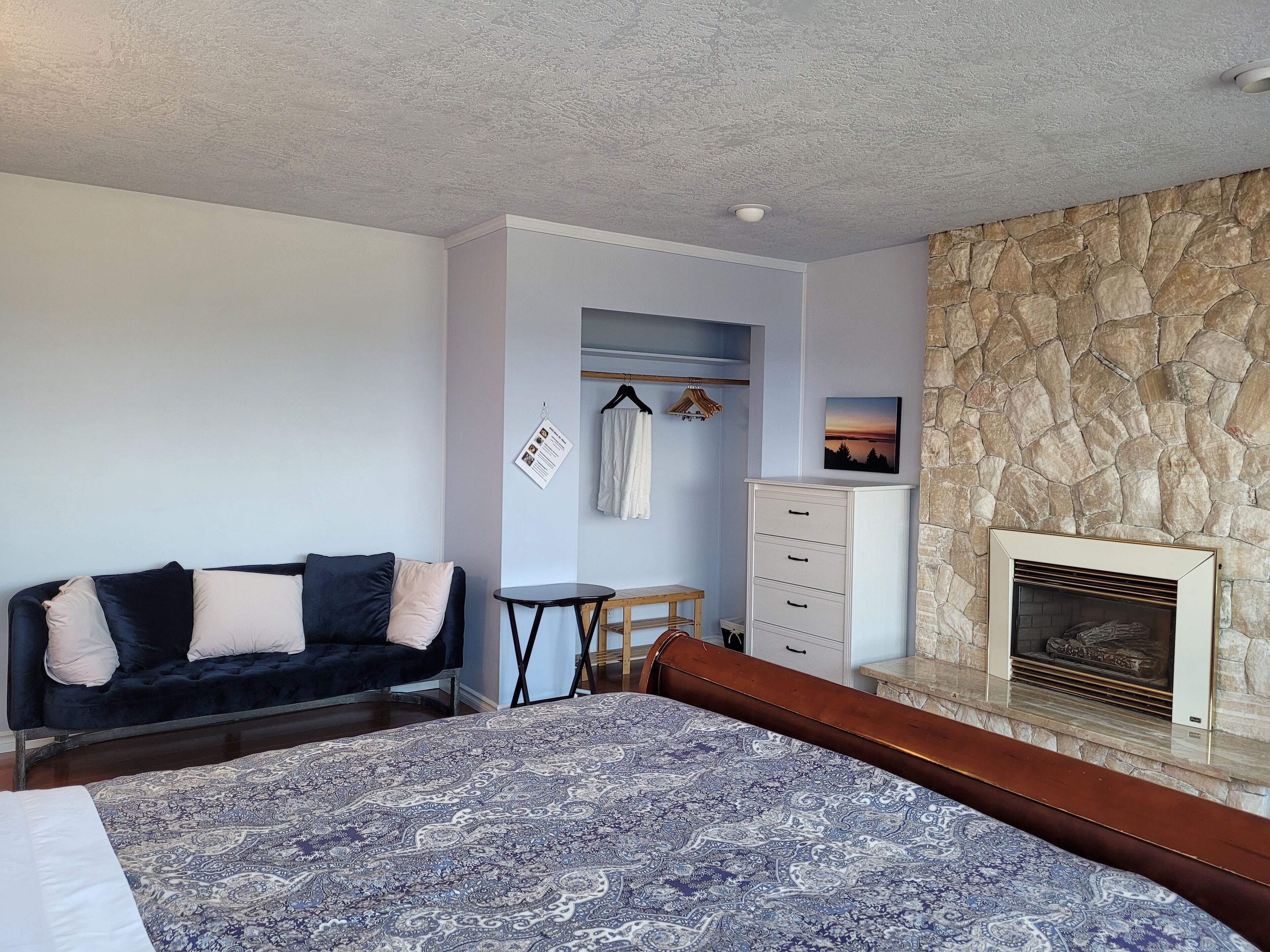 Une chambre avec un grand lit, un canapé bleu foncé, une petite table, une commode et un mur en pierre avec une cheminée.