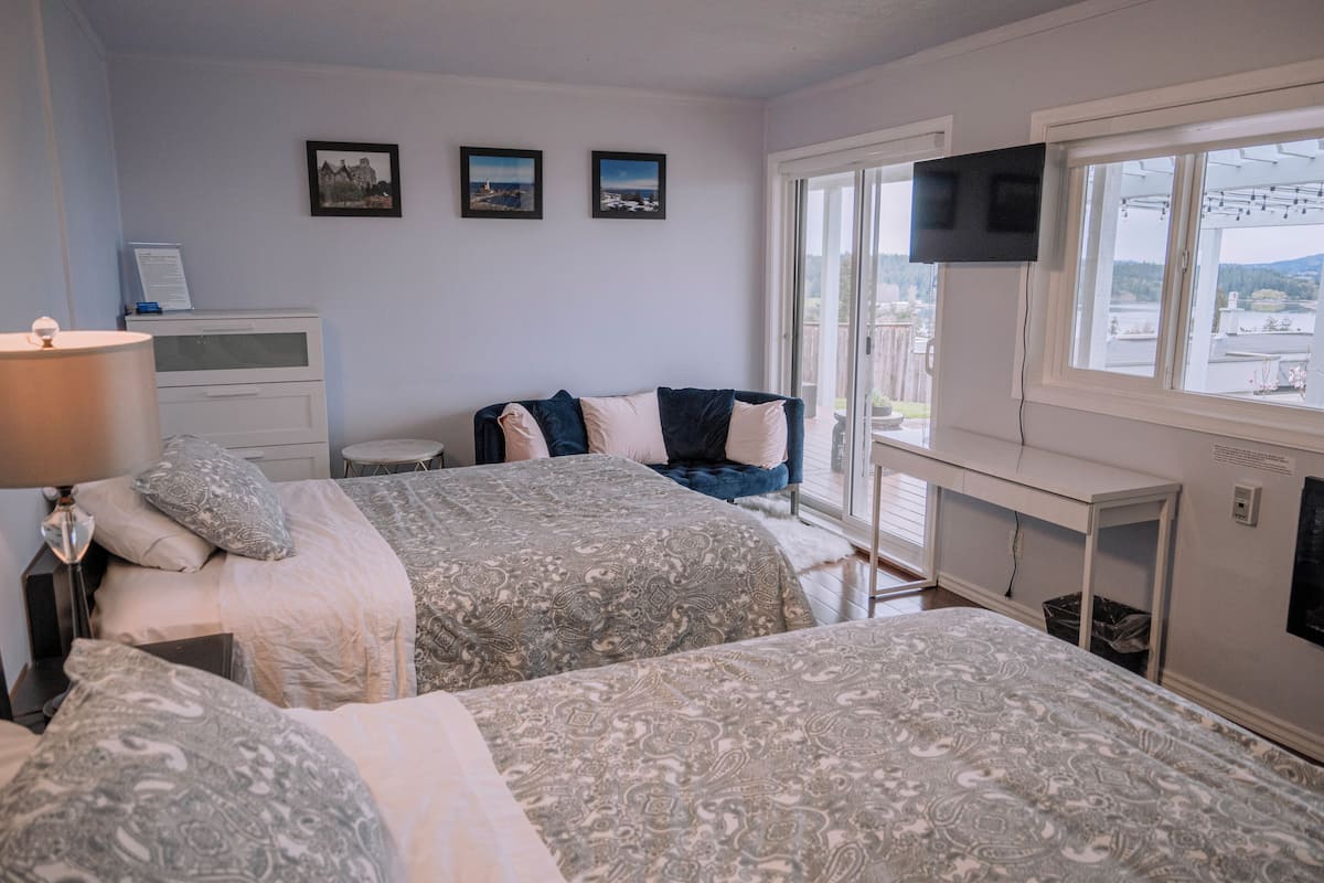 A bedroom with two beds, a desk, a TV, and a window with a view.