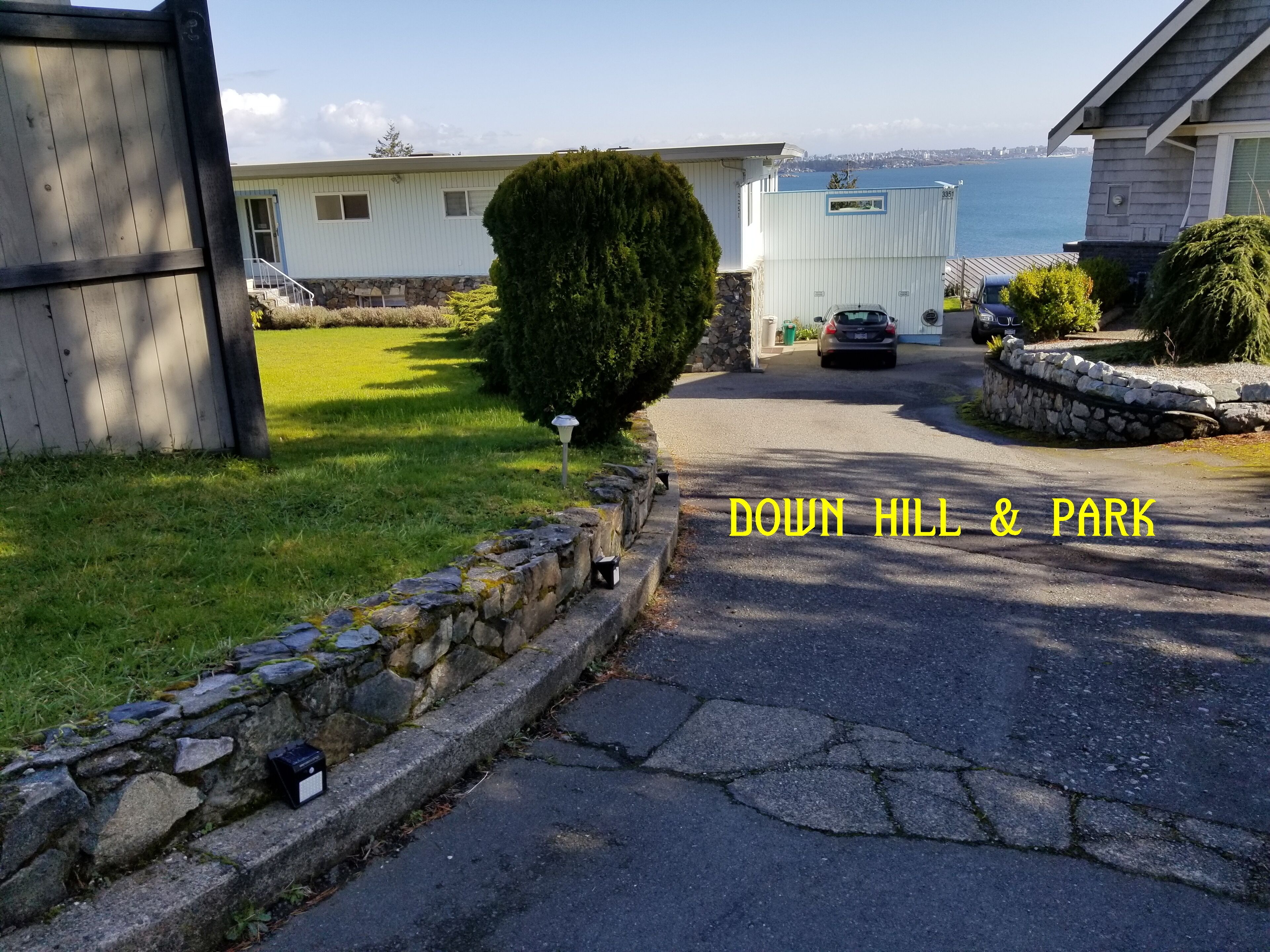 Un quartier résidentiel doté d’un mur en pierre, d’une allée pavée et offrant une vue sur une étendue d’eau au loin.
