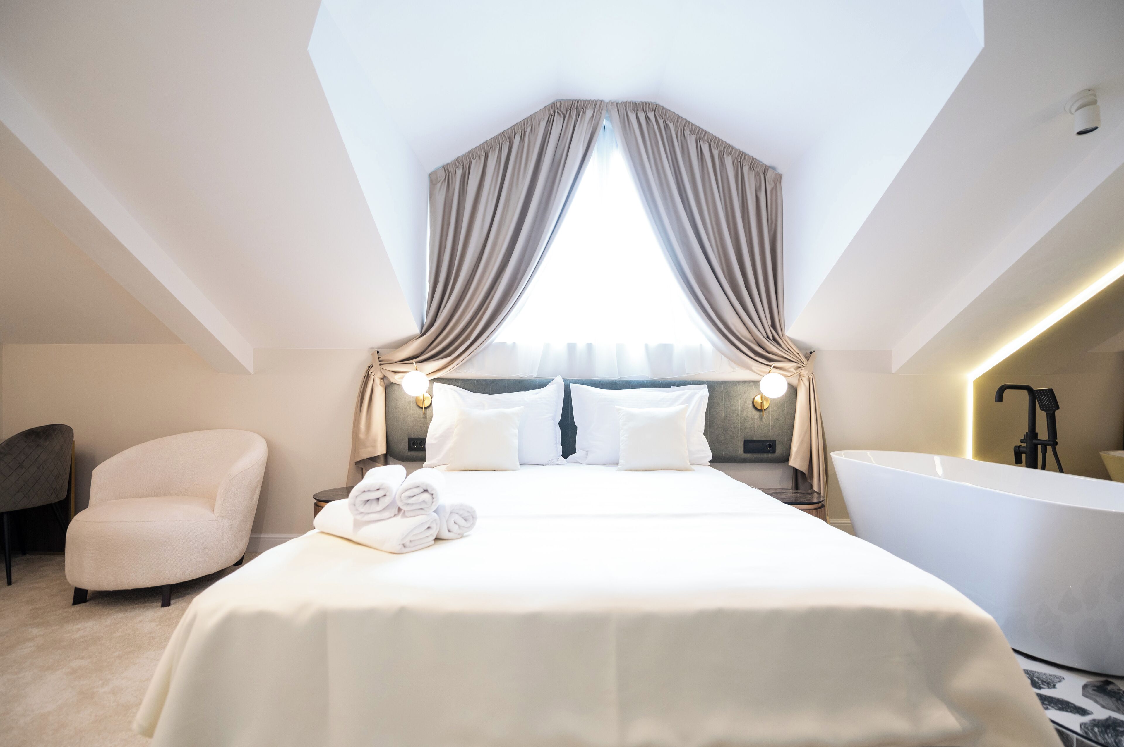 A modern hotel room with a large bed, a sitting area, and a bathtub.