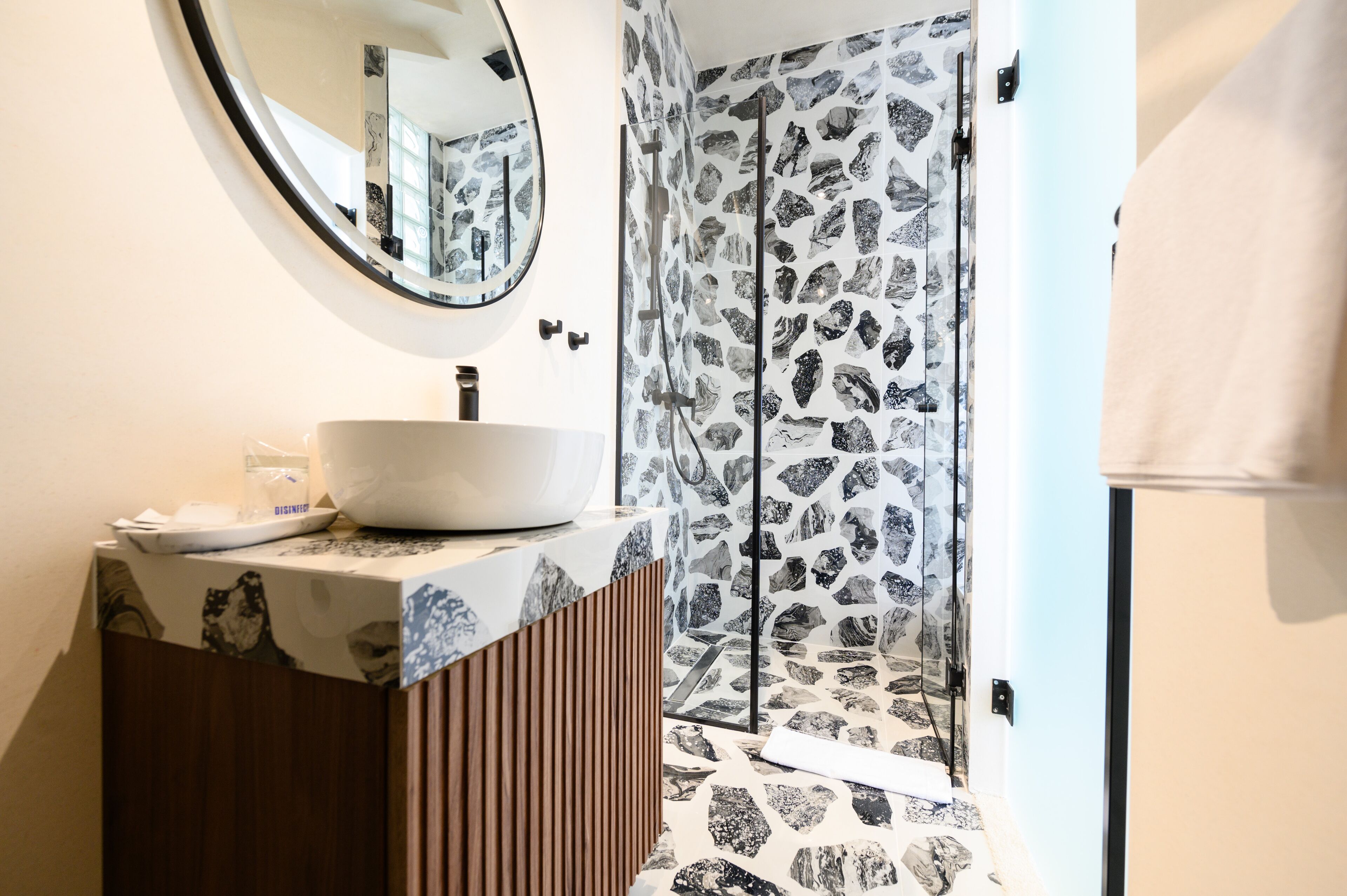 A bathroom with a round mirror, a white sink, and a shower with a patterned wall.