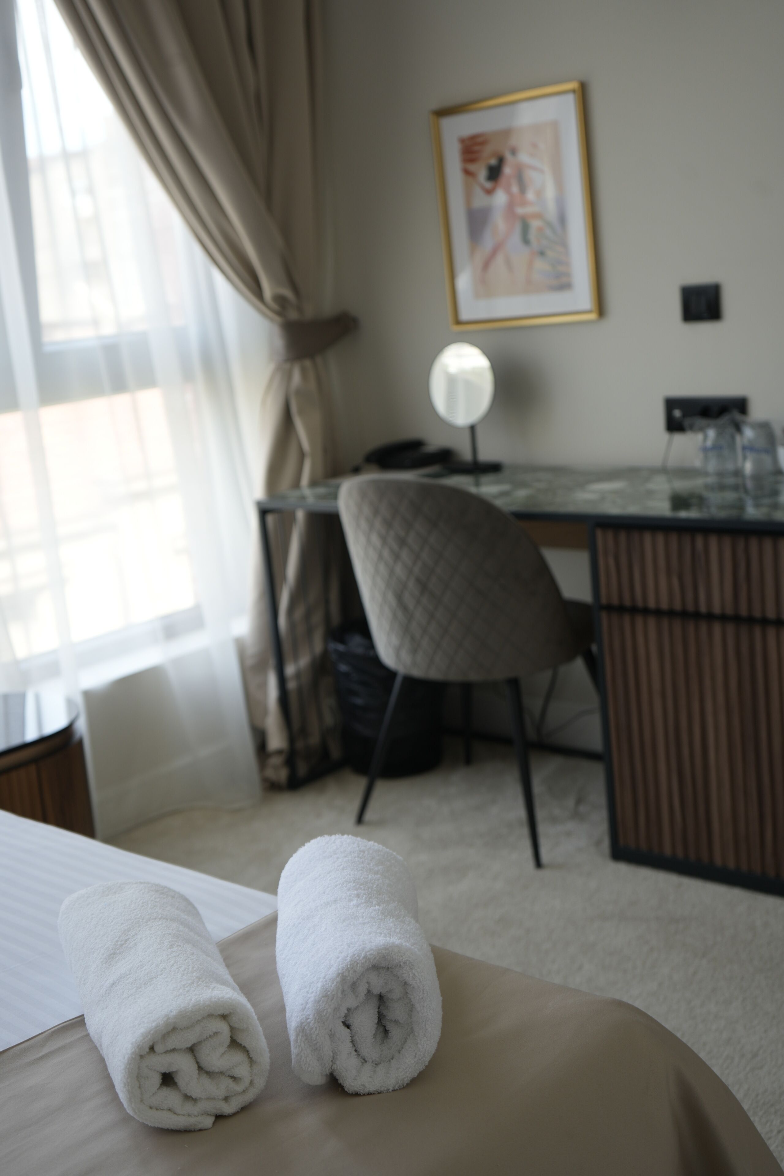 Une chambre d’hôtel avec un lit, deux serviettes roulées, un bureau, une chaise, une lampe et un tableau encadré au mur.