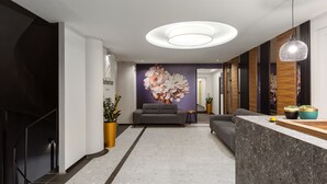 Un lobby moderno con mostrador de recepción, sofás, un gran mural floral y plantas en macetas.