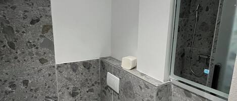 A small bathroom with a toilet, sink, and mirror. The walls are covered in gray stone tiles.