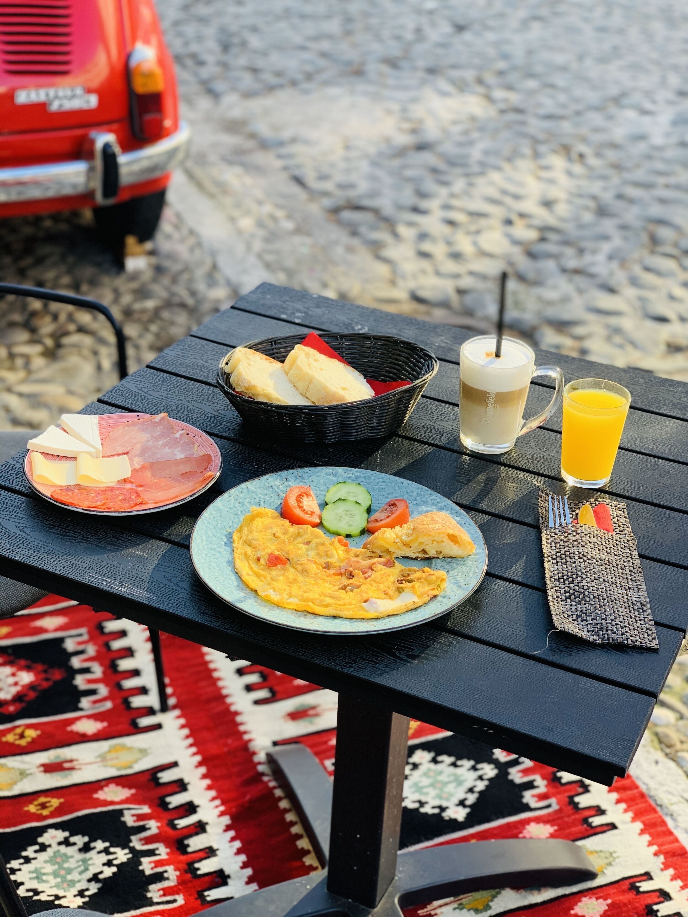 Une table dressée avec des aliments pour le petit-déjeuner, notamment des toasts, des œufs et du jus, posée sur un tapis à motifs.