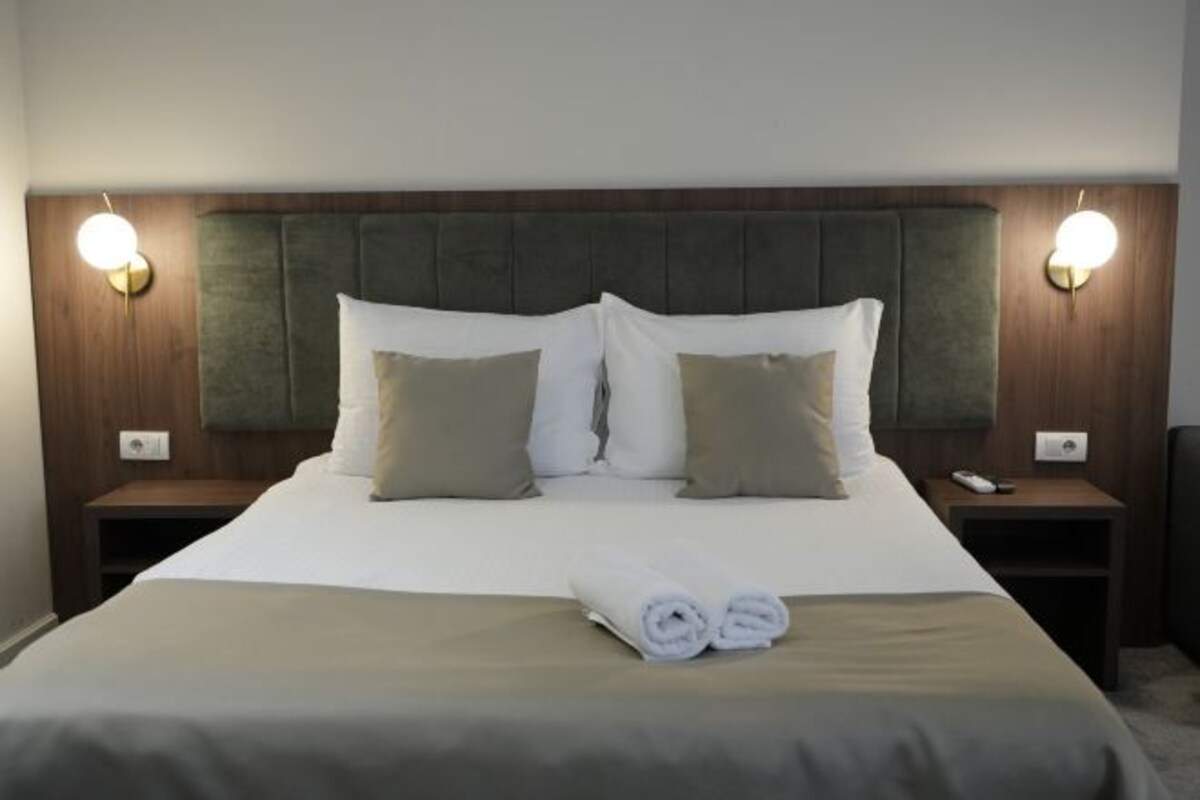 A neatly made bed with a grey headboard, two bedside tables with lamps, and a folded towel on the bed.