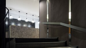 Una escalera moderna con barandilla de vidrio que lleva a una habitación con pared estampada e iluminación colgante.
