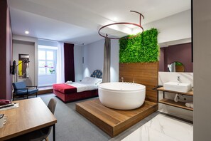 A modern hotel room with a large bathtub, a wooden platform, a green wall, a wooden vanity, and a bed with red bedding. - Hotel Bohemian Garni - Skadarlija (Belgrade)