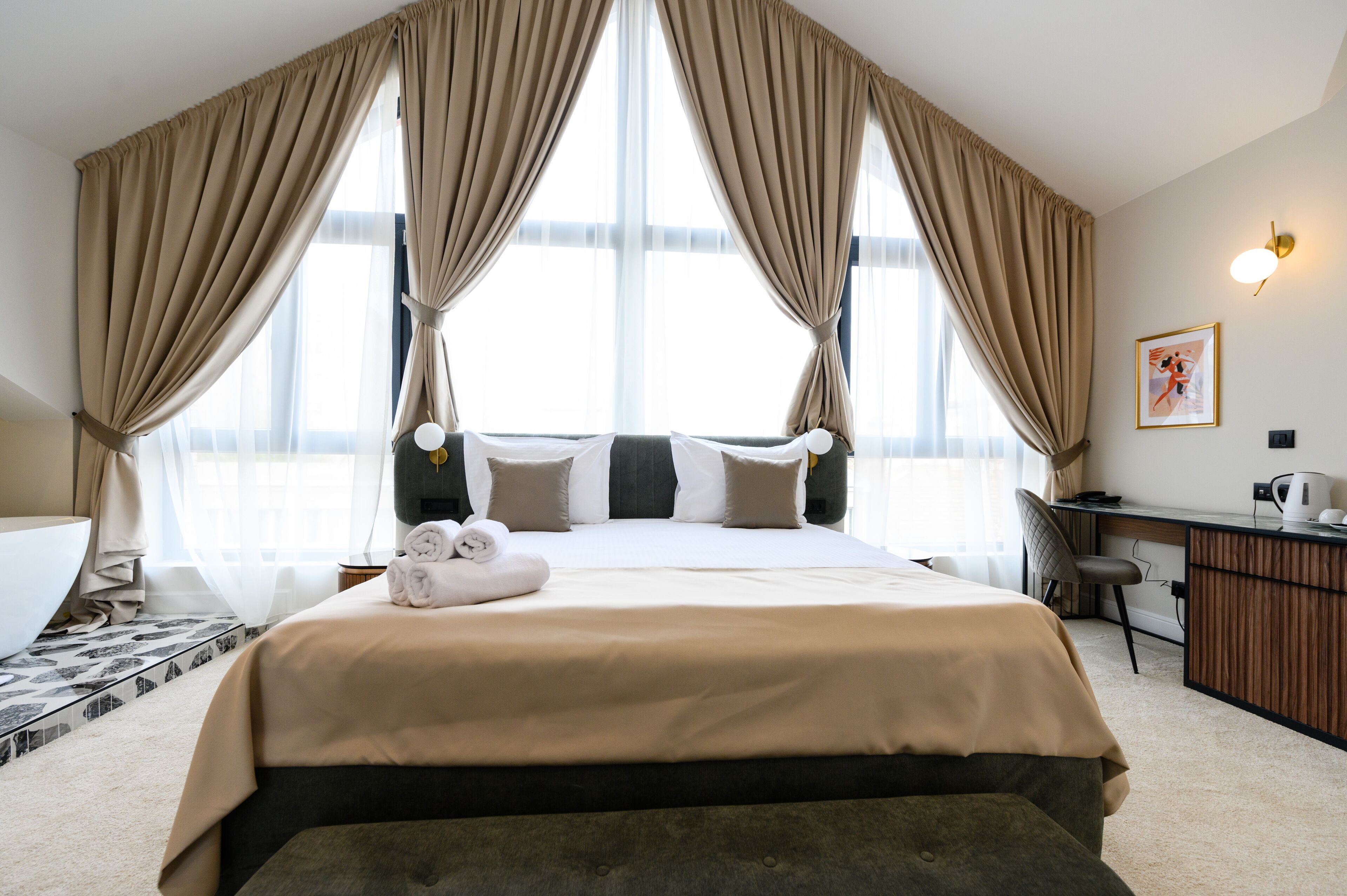 A hotel room with a large bed, a desk, a chair, a bathtub, and a large window with curtains.