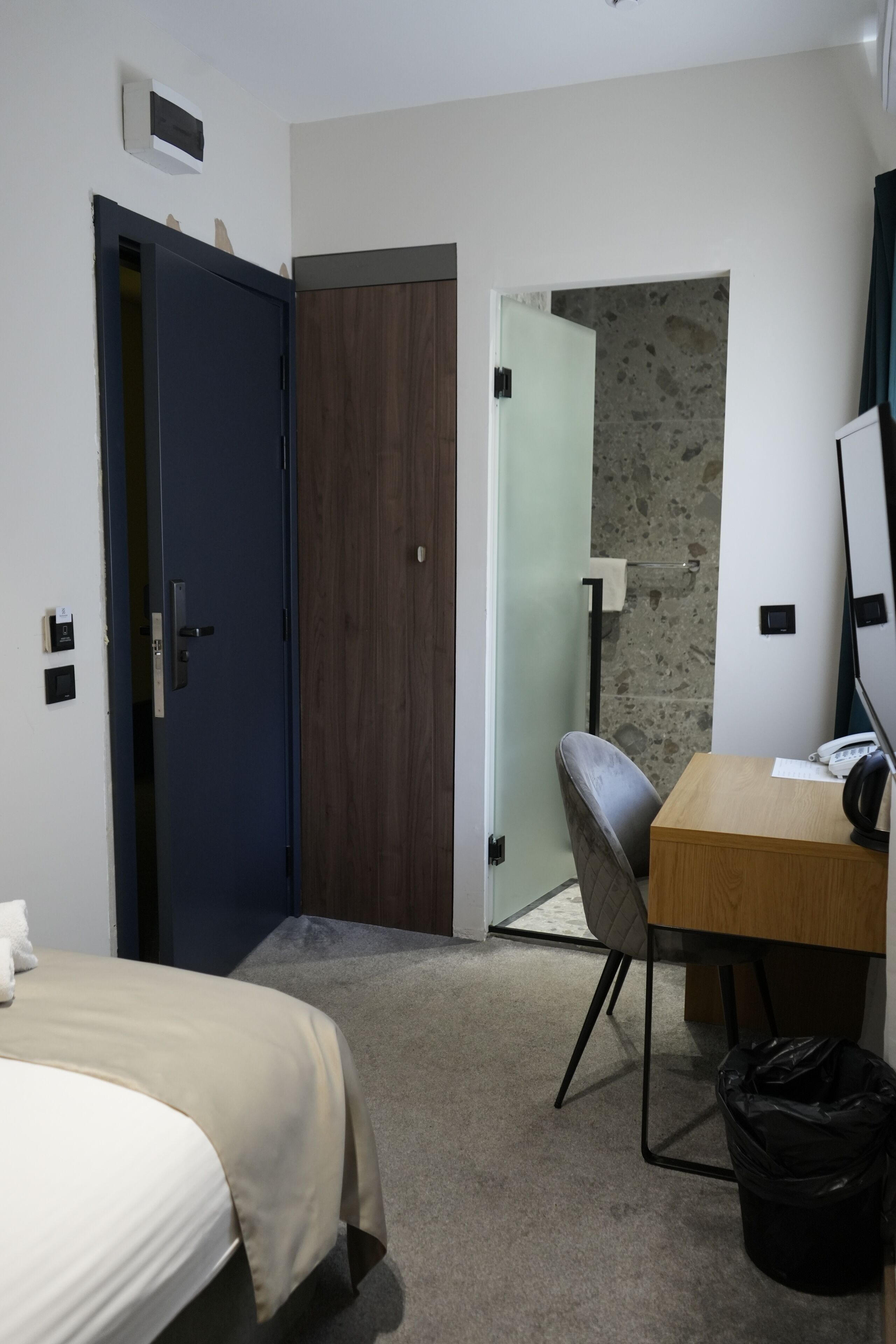 Ein Hotelzimmer mit Bett, Schreibtisch, Stuhl, Computer und Mülleimer.