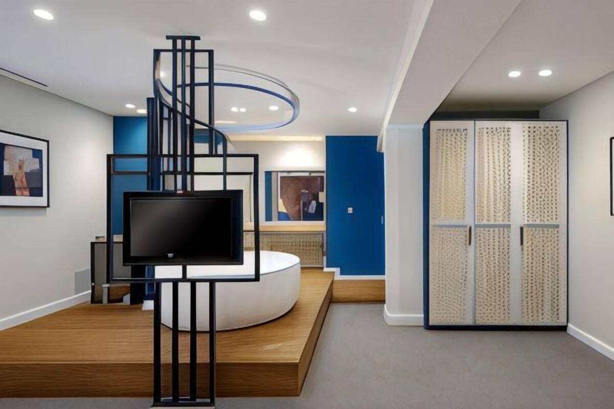 A modern interior with a central circular seating area, a flat-screen TV, and a spiral staircase.