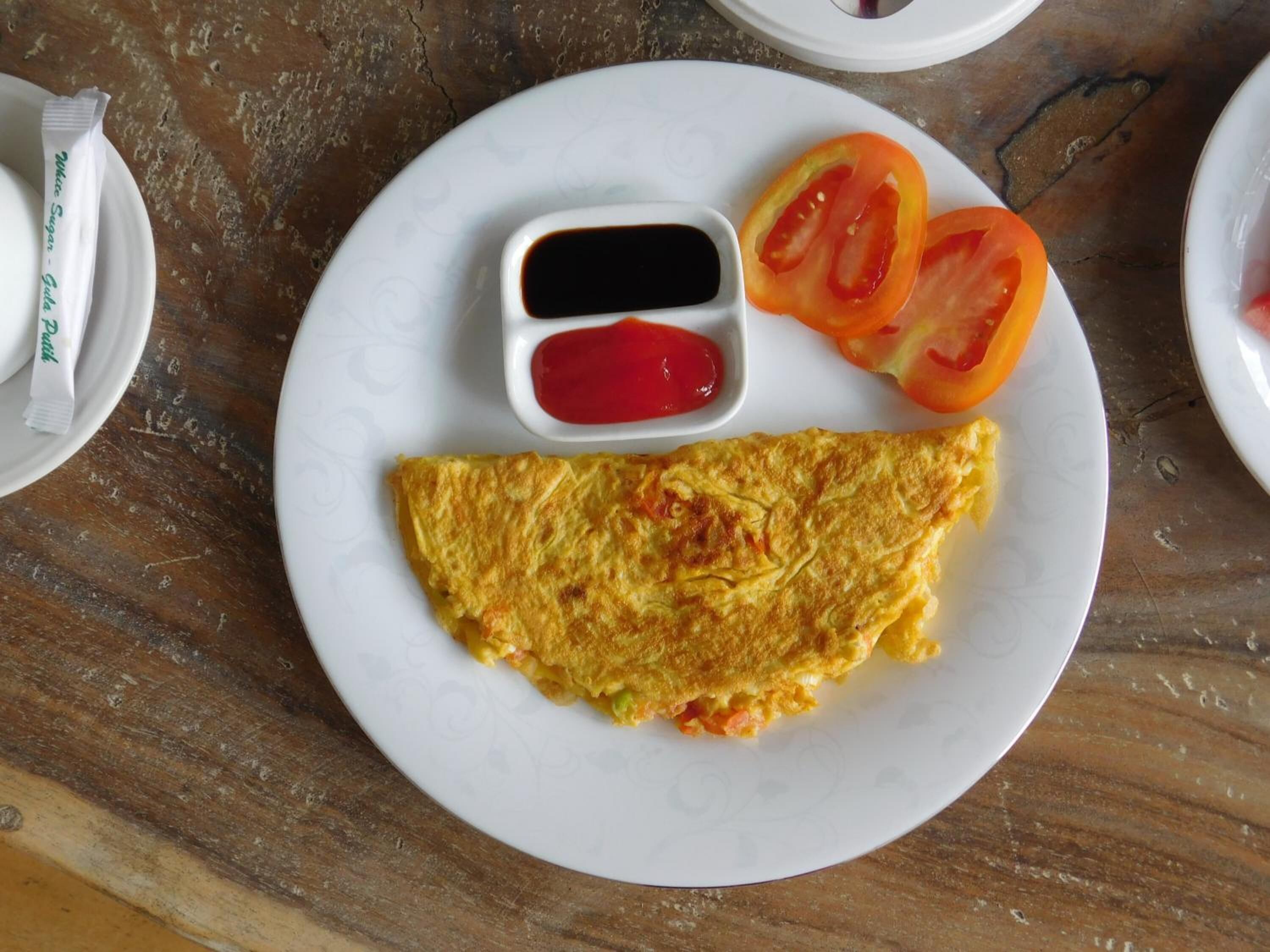 Um prato com omelete, fatias de tomate e dois molhos sobre uma mesa de madeira.