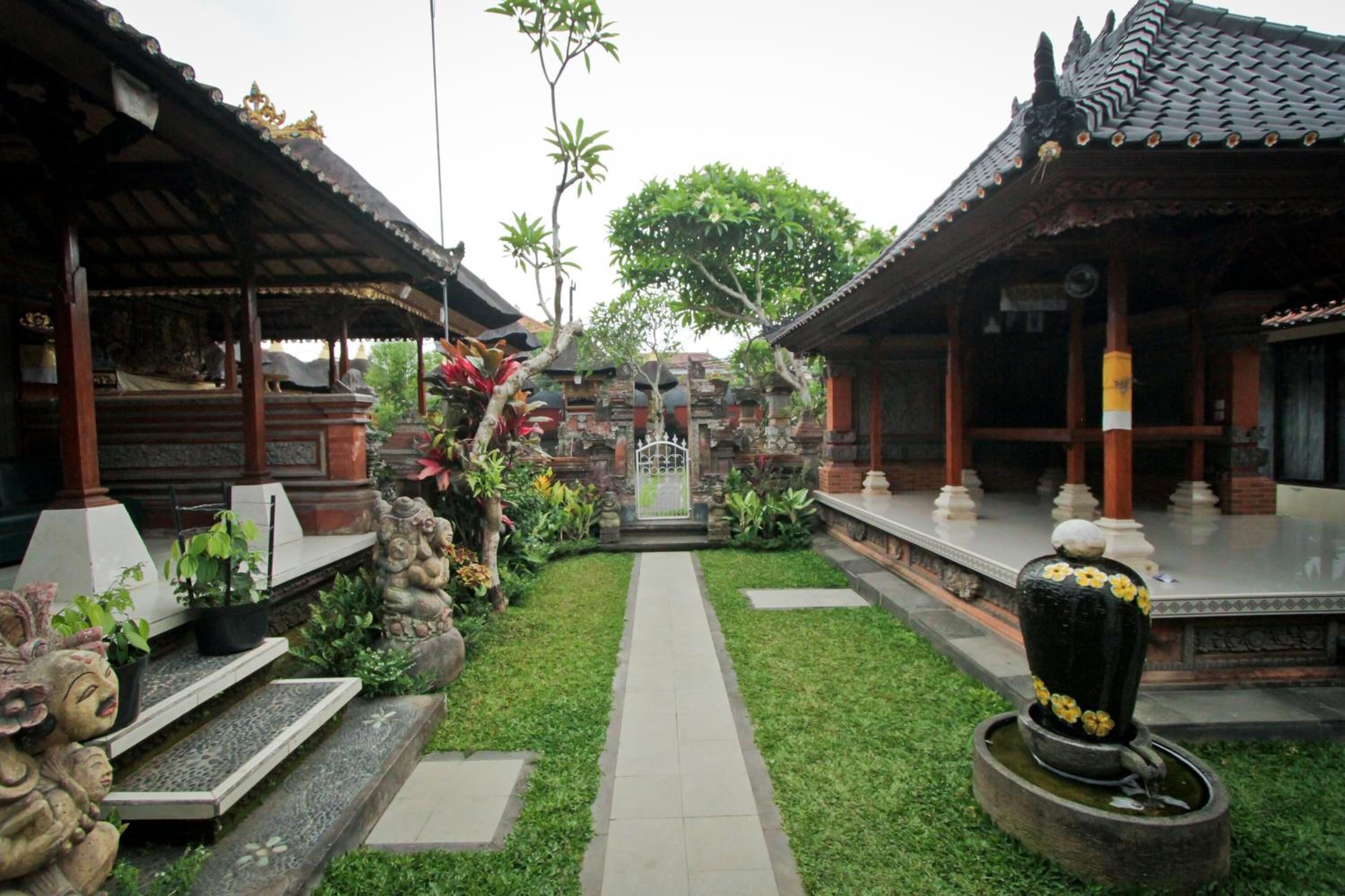 A traditional Balinese temple courtyard with a central pathway, stone steps, and a water feature.