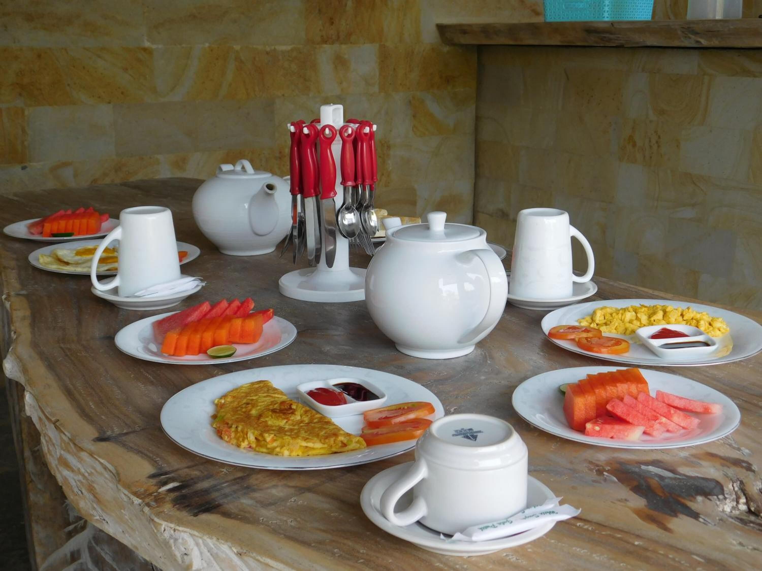 Un bufé de desayuno con diversos platos, teteras blancas y utensilios sobre una mesa de mármol.