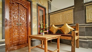 A wooden table and bench in a room with a large intricately carved wooden door and a stone fireplace. - Awan Bali House (Ubud)