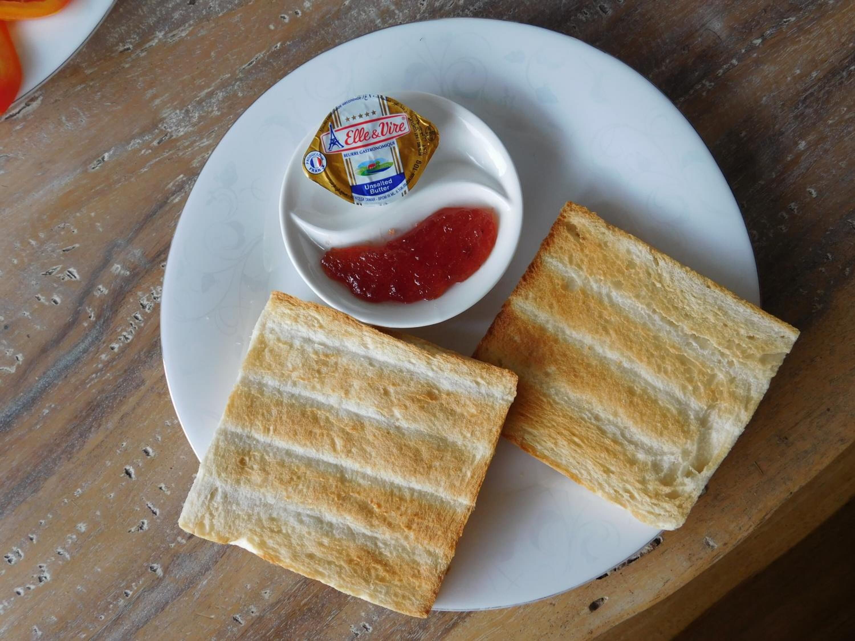 A plate with two slices of toasted bread, a small bowl of unsalted butter, and a small bowl of red jam.