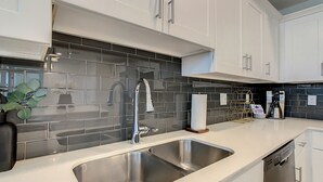 Una cocina moderna con armarios blancos, un lavamanos de acero inoxidable y un salpicadero de azulejos negros.