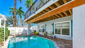 A pool area with a wooden deck, lounge chairs, and a covered patio.
