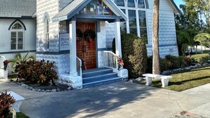 A church with a steeple, a porch, and a large palm tree in the front yard.