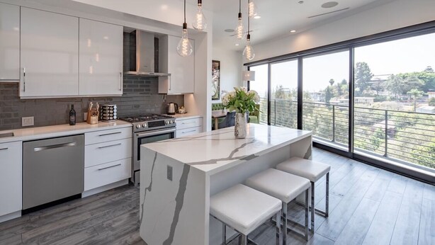 Una cucina moderna con mobili bianchi, un'isola in marmo e un'ampia finestra con vista sulla città.