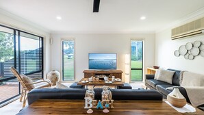 Ein geräumiges Wohnzimmer mit großem Fernseher, einem Holztisch und einer Couch.
