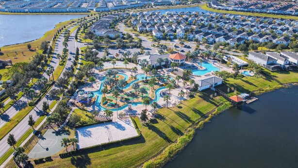 An aerial view of a residential area with a large swimming pool, multiple houses, and a body of water.