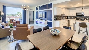 A modern living room with a dining table, sofas, and a kitchen area with white cabinets and a microwave.
