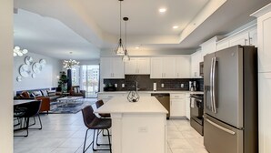 A modern kitchen with white cabinets, a large island, stainless steel appliances, and a dining area with a sofa and chairs.