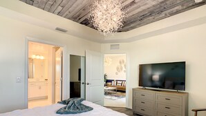A bedroom with a large bed, a TV, a dresser, and a chandelier.