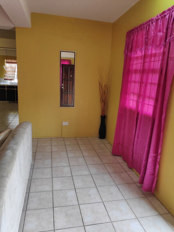 A room with yellow walls, a tiled floor, a window with a pink curtain, and a potted plant.