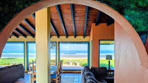 Eine überdachte Terrasse mit Blick auf den Strand, ausgestattet mit einer Couch, Stühlen und einem Tisch.