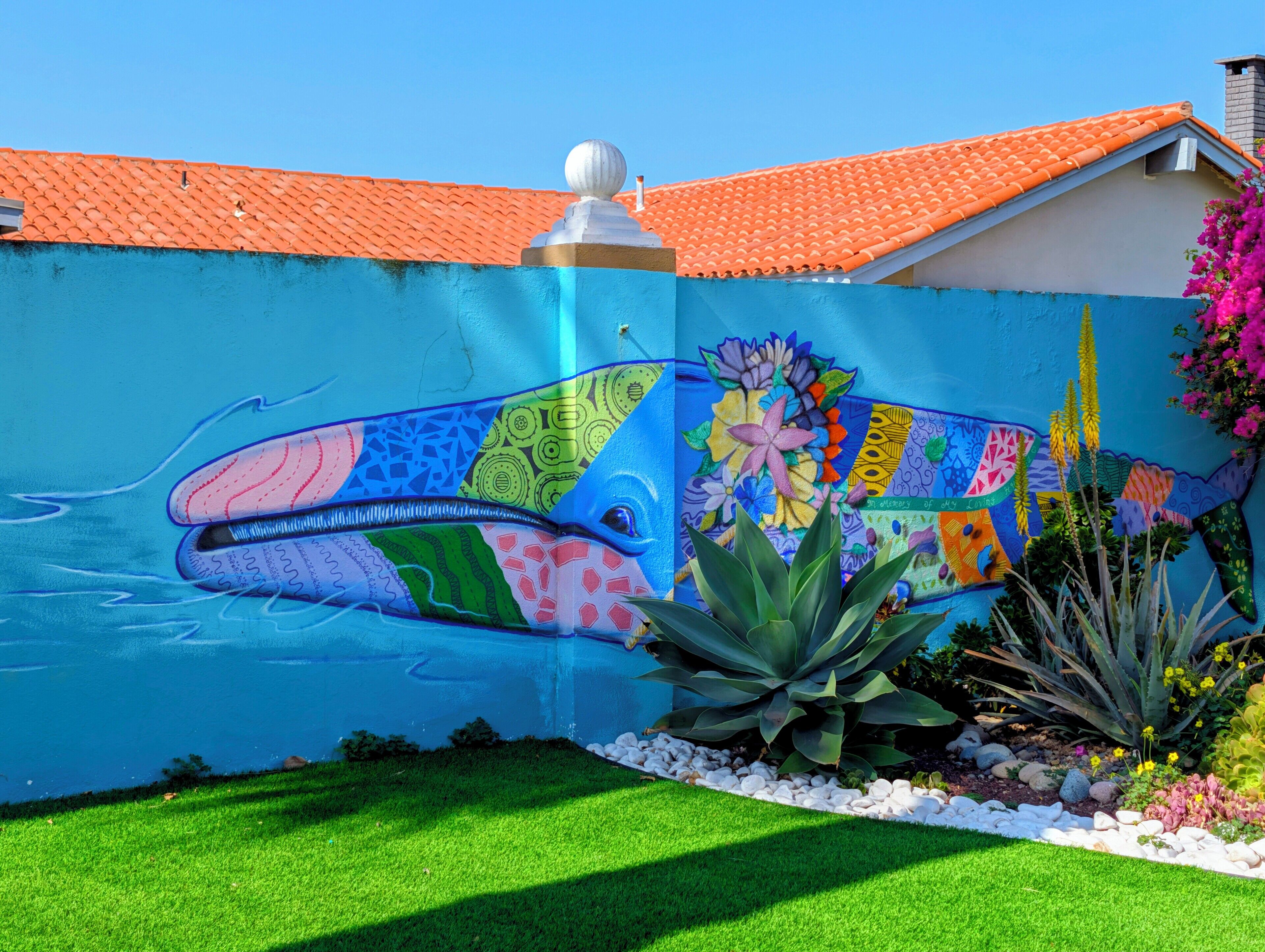 A colorful mural of a whale on a wall, surrounded by a garden with various plants and flowers.