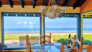 Ein Essbereich mit Holztisch und -stühlen, einer Kristallleuchtre und Blick auf den Strand.