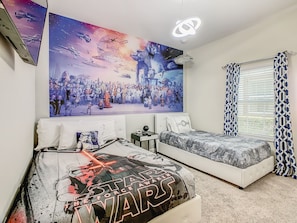 Un dormitorio con decoración temática de Star Wars, que incluye un mural grande, una cama con manta de Star Wars y una almohada de Star Wars.