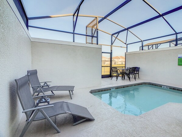 An indoor swimming pool with lounge chairs and a table, surrounded by a glass enclosure.