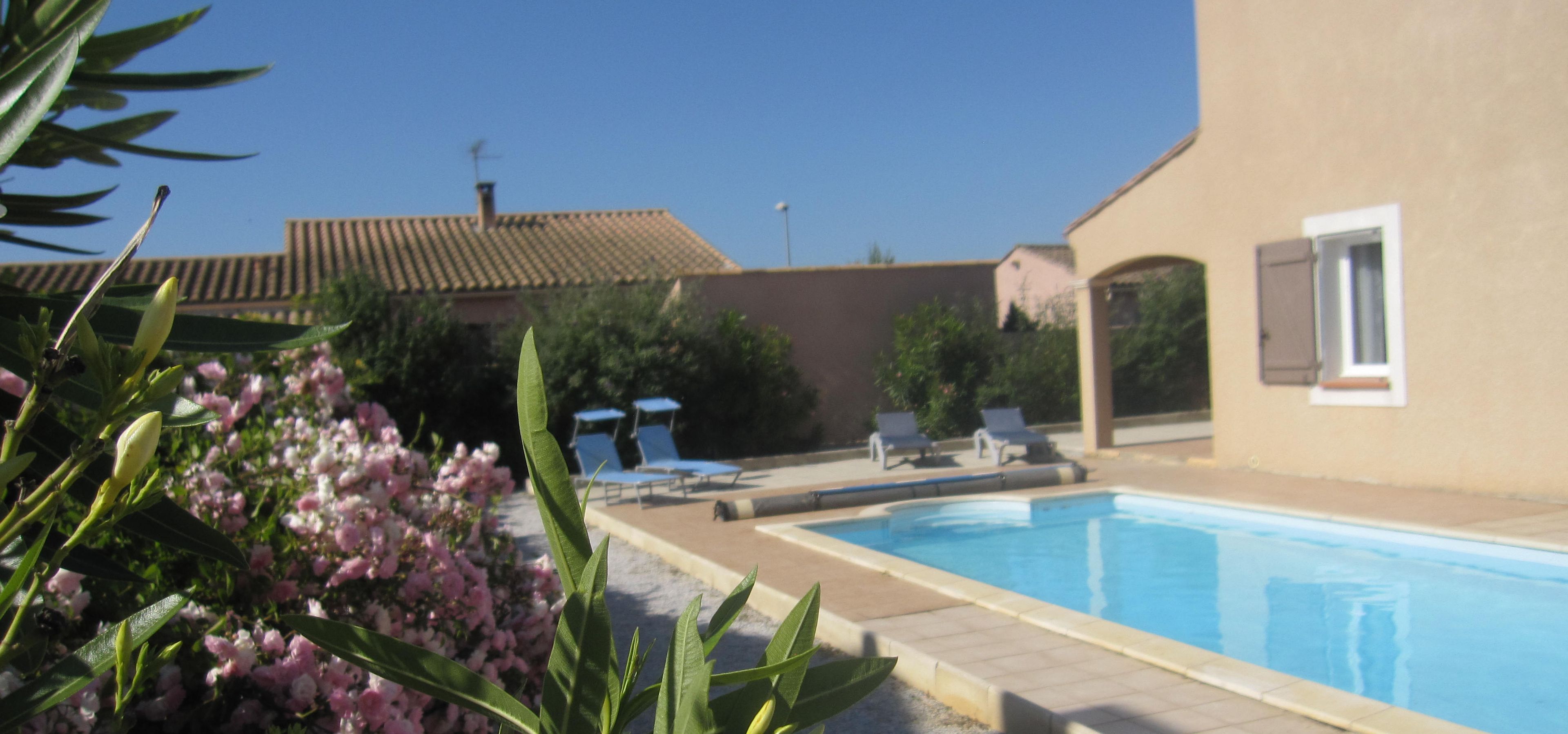 A swimming pool with lounge chairs, surrounded by greenery and a building with a tiled roof.