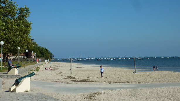 Une plage avec un ciel dégagé, quelques personnes et des bateaux sur l’eau.