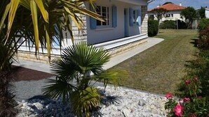 Une maison de plain-pied à l’extérieur blanc et aux bordures bleues, entourée d’une pelouse bien entretenue et d’une variété de plantes.