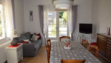 Un salon comprenant un canapé, une table à manger, des chaises, un téléviseur et une lampe.