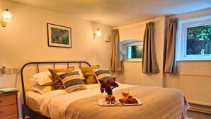 A neatly made bed with a decorative headboard, a bedside table with a book, and a window with curtains. - Garden Apartment- perfectly located (Shanklin)