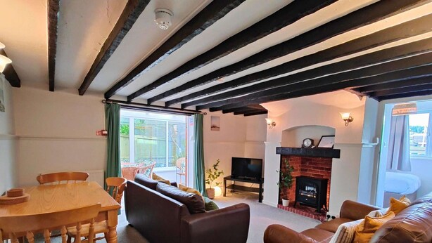 A living room with a fireplace, a television, and a dining area with a table and chairs. - Garden Apartment- perfectly located (Shanklin)