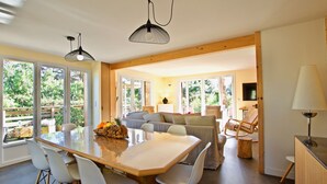 Een ruime woonkamer met een houten eettafel, witte stoelen, een bank en een televisie.
