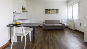A modern kitchen with white cabinets, a dining table, and a gray sofa.